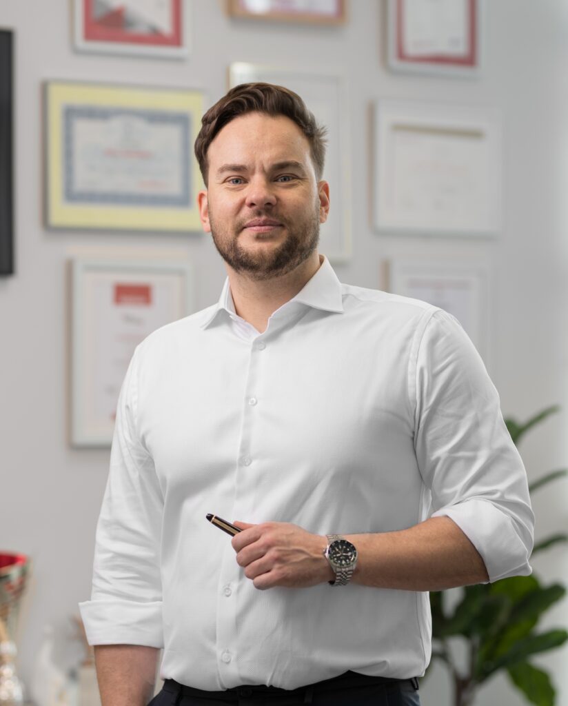 Mężczyzna w koszuli stojący w pokoju pełnym dyplomów